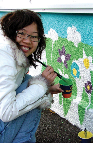 Asian girl knealing down with a pot of green paint smiling at the camera